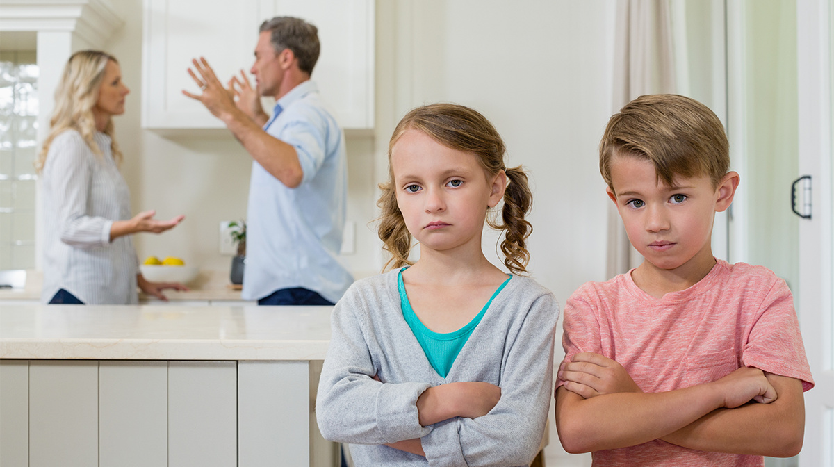 A sad girl and boy standing in front of arguing parents